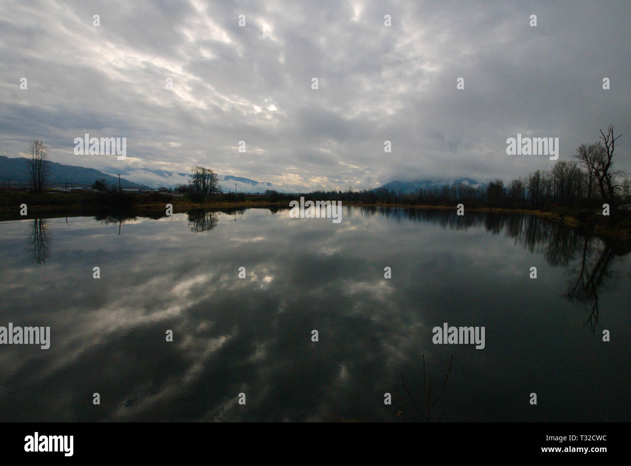 Una placida backwater del fiume di Vedder riflette un cielo grigio turbolento coperto in Chilliwack, Columbia Britannica, Canada Foto Stock
