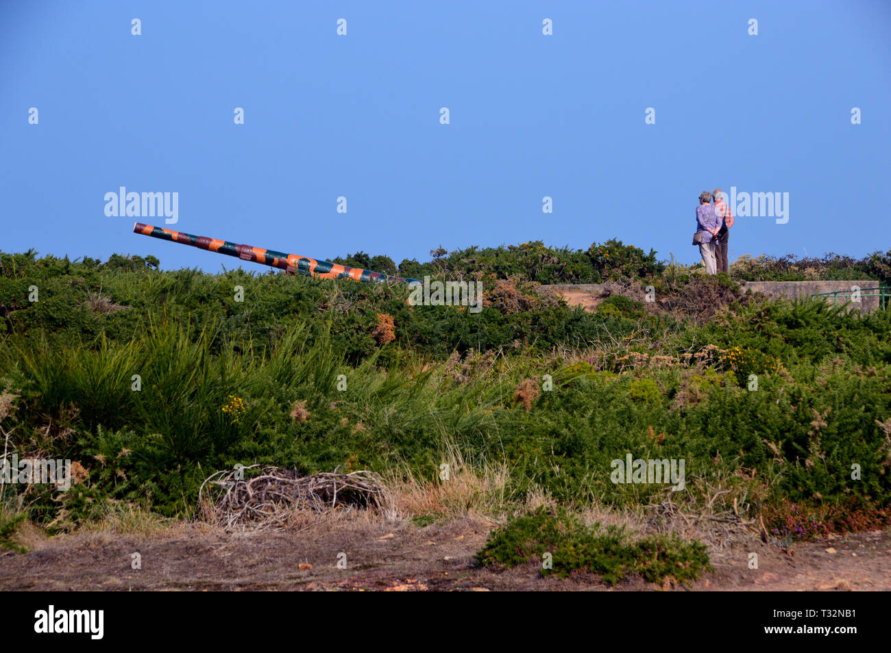 Una Coppia Matura di vacanzieri guardando il mimetizzata WW2 artiglieria tedesca pistola a Les Landes sull'isola di Jersey, nelle Isole del Canale, UK. Foto Stock