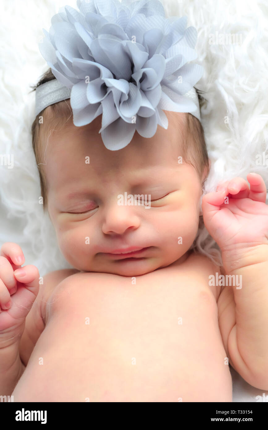 Close up di un sonno neonato indossare una fascetta con un grande fiore di  colore grigio, appoggiando la sua testa su una pelliccia bianca cuscino  Foto stock - Alamy