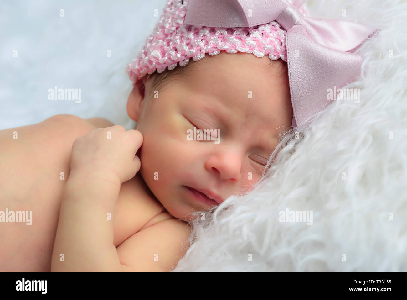 In prossimità di un grazioso neonato ragazza dorme su una pelliccia bianca cuscino indossando un rosa Berretto in maglia con grande fiocco rosa Foto Stock