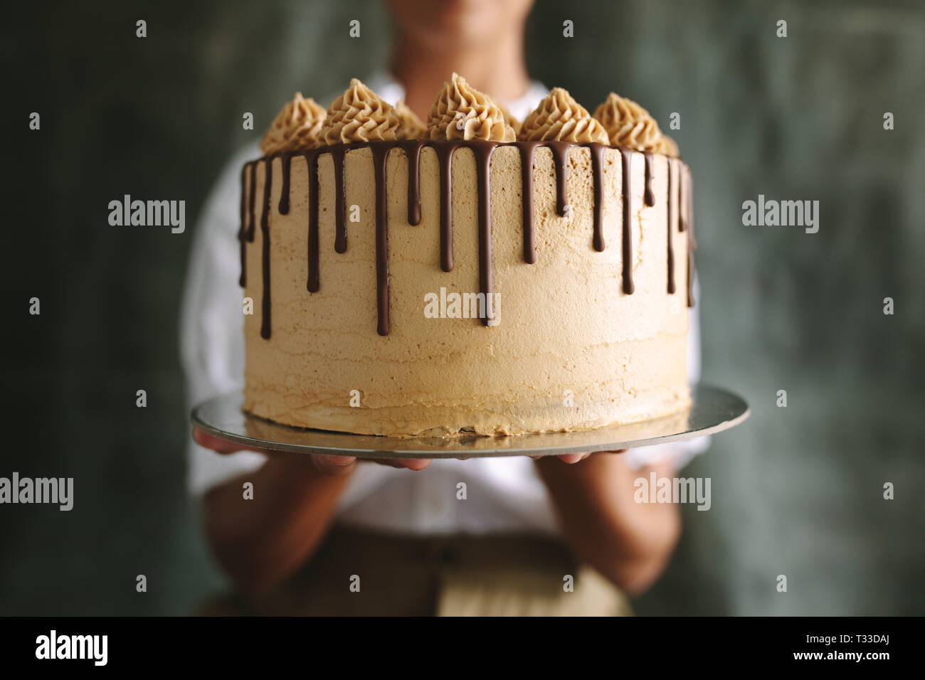 Close up di chef femmina holding torta. Baker che mostra una gustosa torta contro uno sfondo grigio. Foto Stock