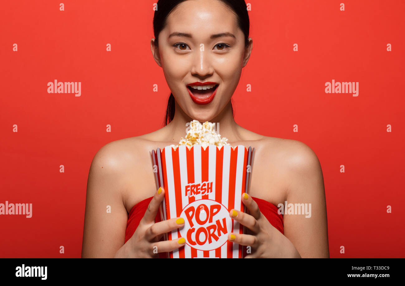 Ritratto di bella donna asiatica con un popcorn su sfondo rosso. Excited donna pronta per guardare film. Foto Stock