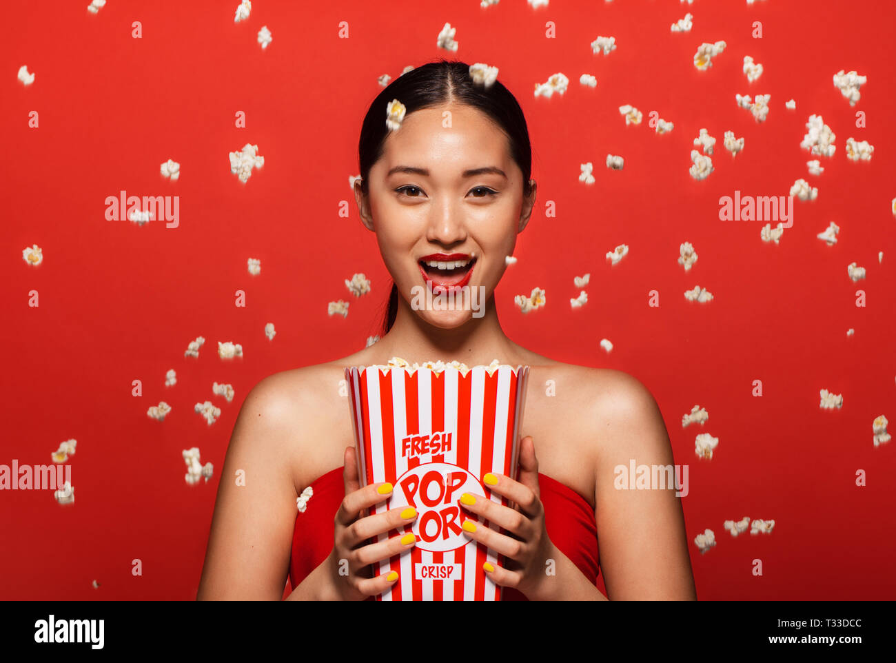 Ritratto di donna eccitata con popcorn volare su sfondo rosso. Femmina di guardare un film. Foto Stock