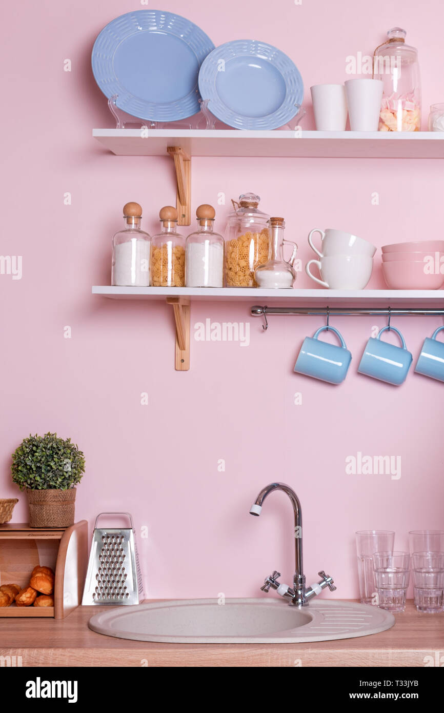 Rosa e blu pastello cucina moderna interni. Accessori da cucina, contenitori con cereali, piatti e appendere tazze blu. Foto Stock