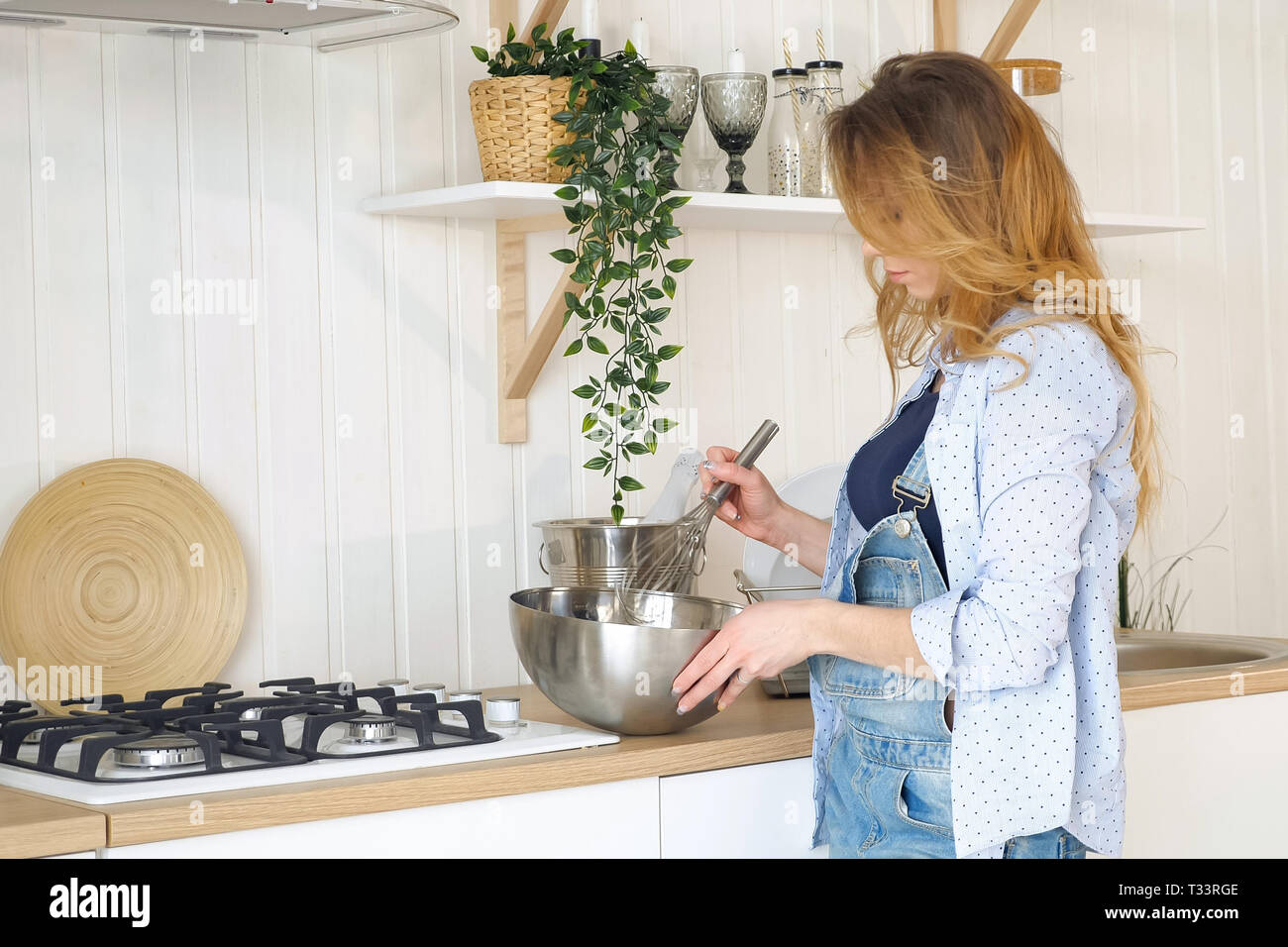 Giovane biondo capelli lunghi accompagna la donna nel recipiente di metallo sul tavolo vicino alla stufa in cucina moderna con piante in vaso Foto Stock