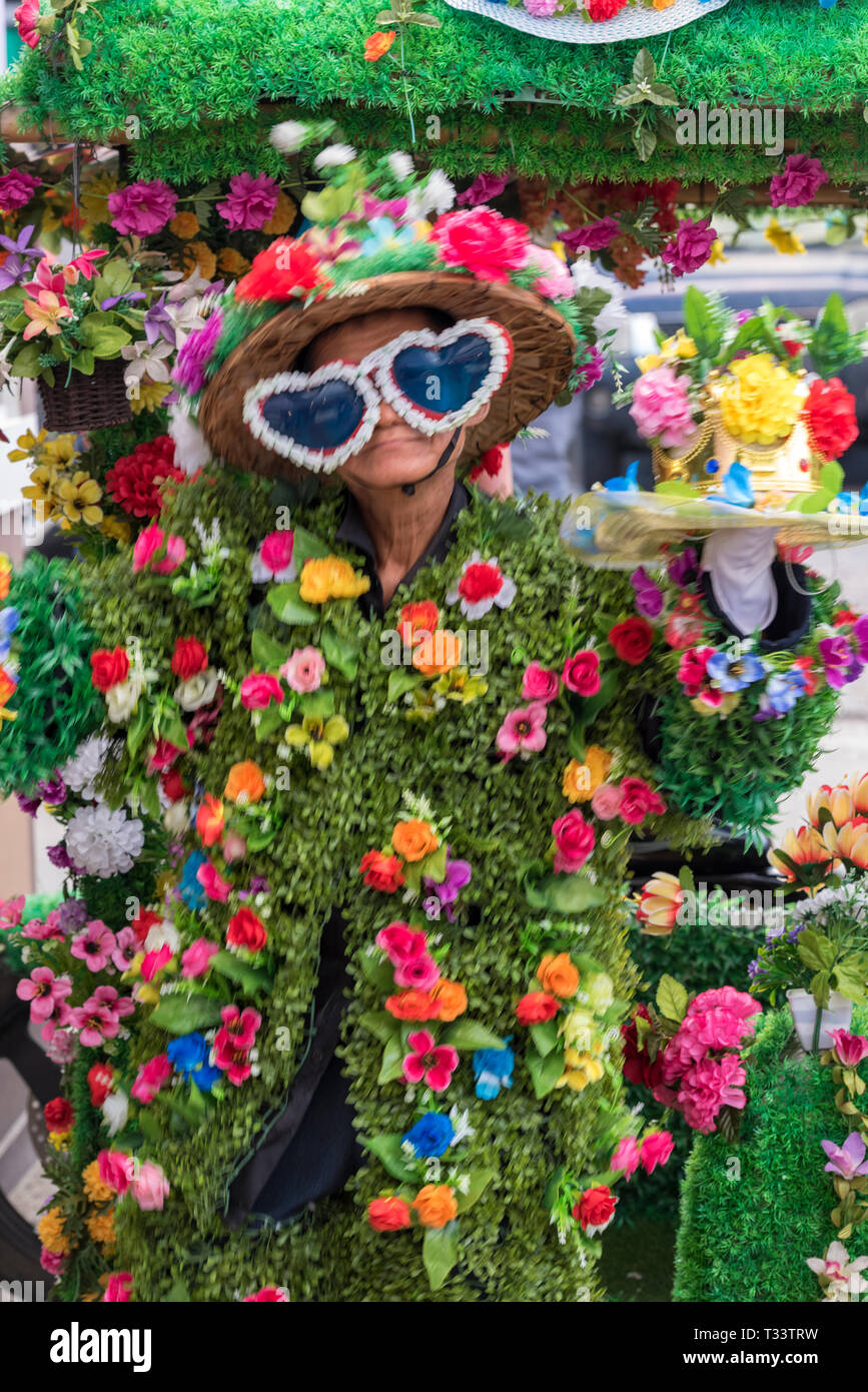 Una persona vestita in un abito botanico tutto sopra fiorito di fiori colorati in un mercato in Thailandia, Asia. Foto Stock