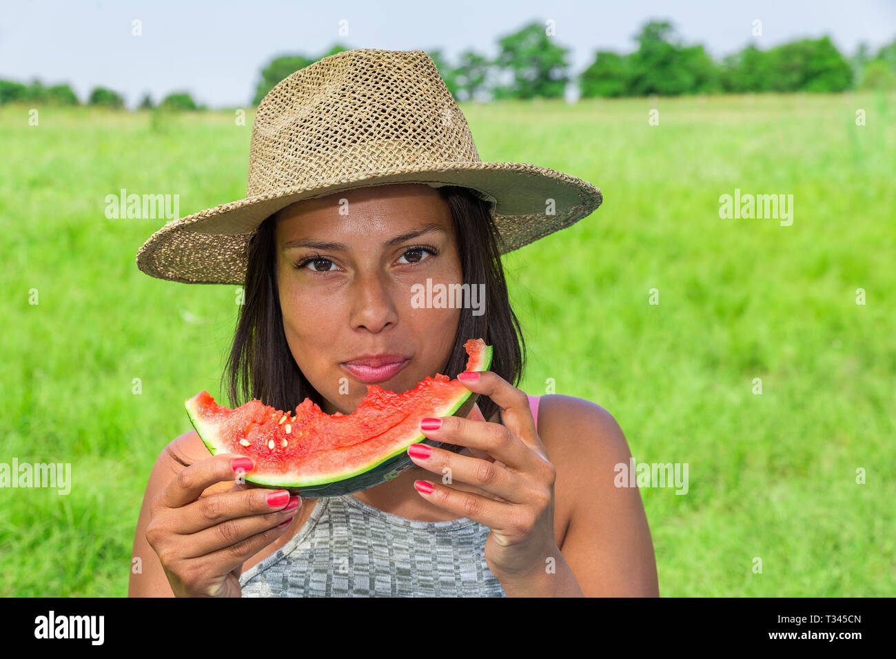 Giovanissimo colombiano donna che indossa la paglia estate hat mangiare fresco melone rosso nella natura olandese Foto Stock