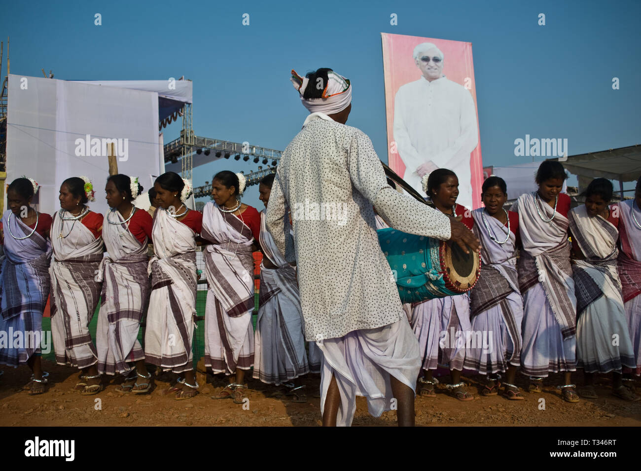 Danzatori tribali e musicista che partecipano ad una fiera locale + Tabellone che rappresenta un politico locale ( India) Foto Stock