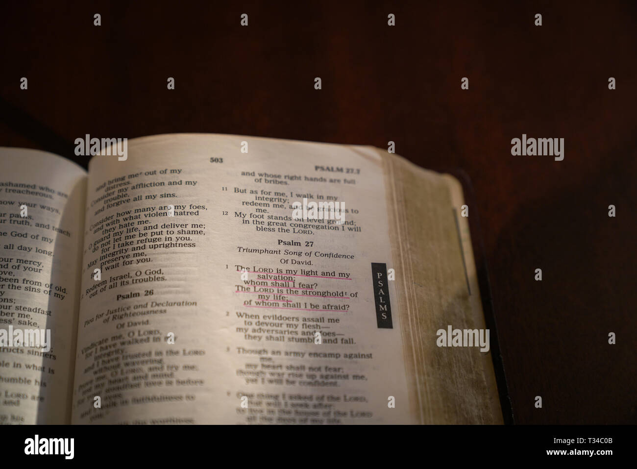 Aprire la bibbia al buio su un tavolo di legno con la luce e la messa a fuoco sul salmo 27 Foto Stock