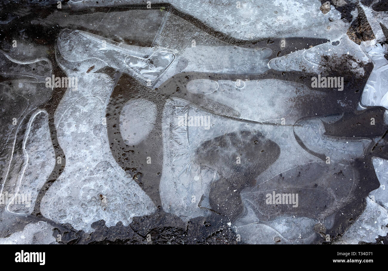 Ghiaccio rotto che ricopre una pozza lungo la strada con aria intrappolata sotto per creare una texture invernale e un motivo che rappresenta l'inverno Foto Stock