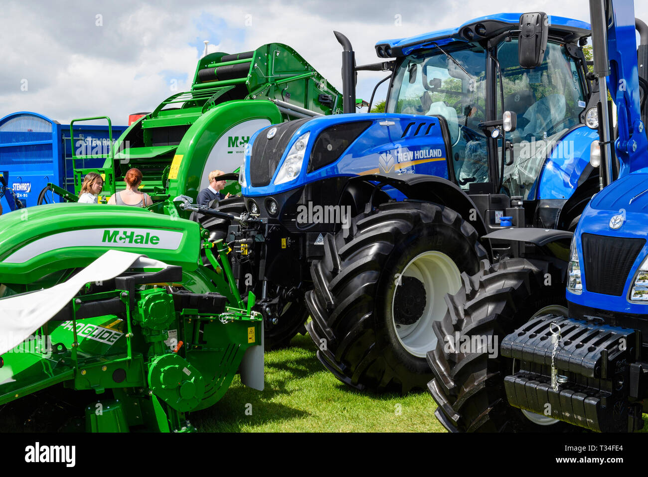 Visualizzazione delle macchine agricole (trattori New Holland, McHale imballatrice & falciatrice) parcheggiato a fianco a fianco sul commercio stand - Grande spettacolo dello Yorkshire, Inghilterra, Regno Unito. Foto Stock