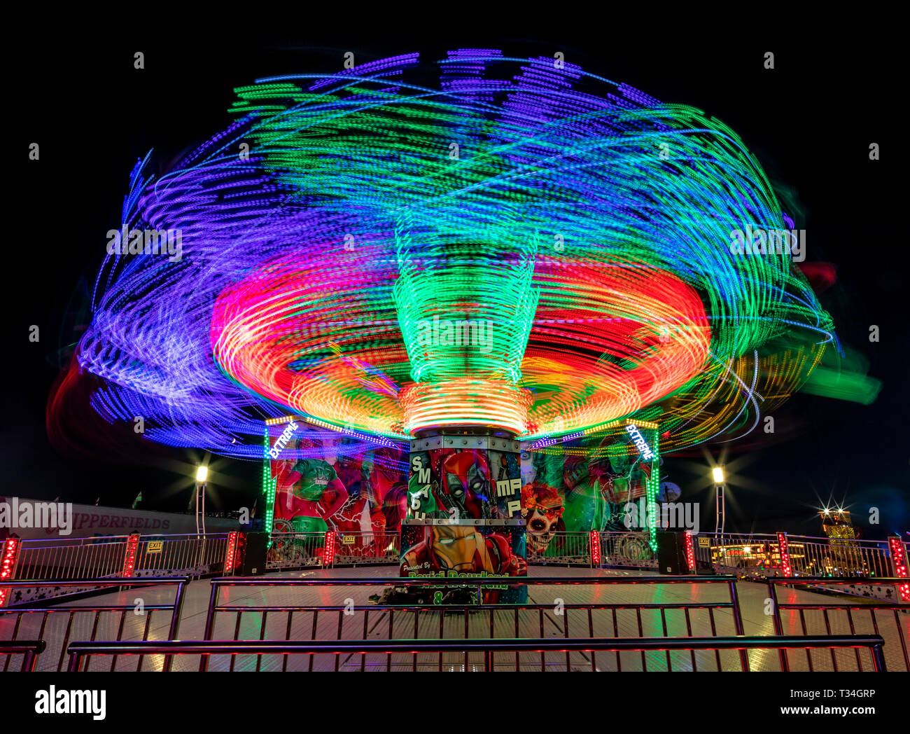 Immagine a lunga esposizione di un giro in fiera di notte, dipingendo vivaci percorsi di luci al neon che si alternano al movimento dinamico e allo stile di vita emozionante. Foto Stock