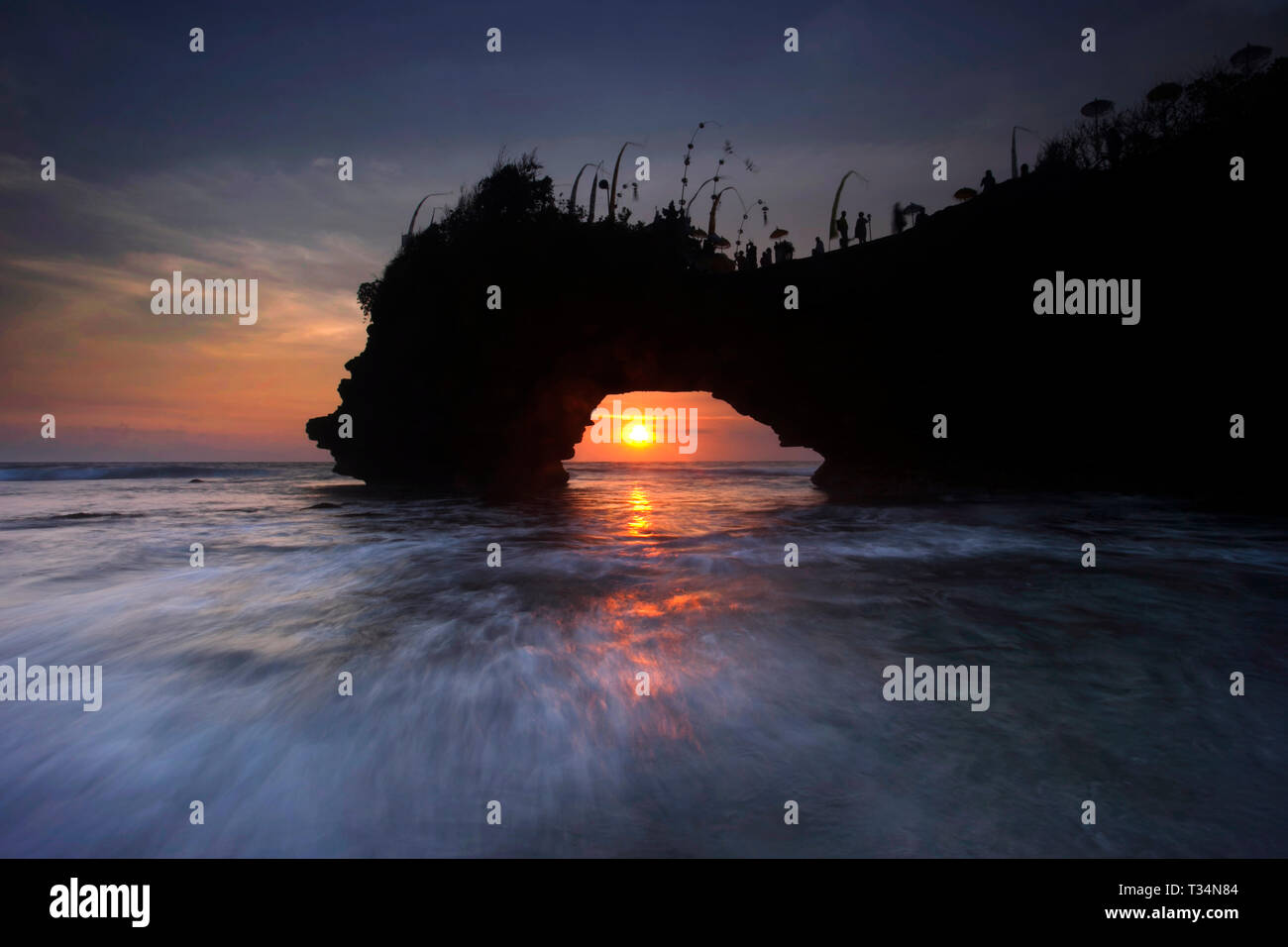 Vista tramonto attraverso un arco roccioso sulla spiaggia, Bali, Indonesia Foto Stock