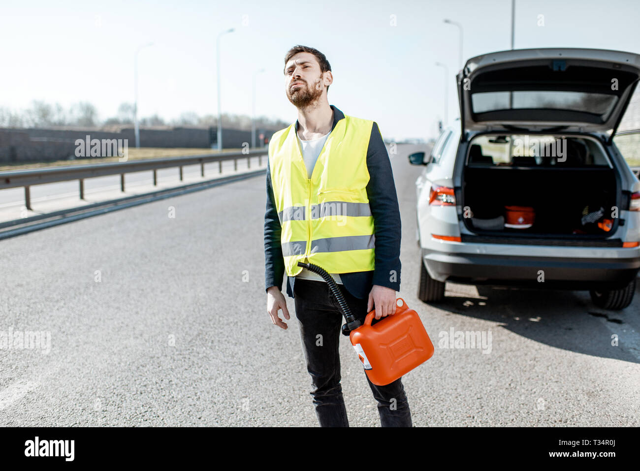 Uomo con la disperazione di emozioni in attesa per l'auto per fare rifornimento di benzina con permanente canister sul ciglio della strada Foto Stock