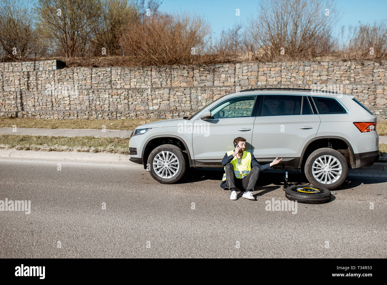 Uomo seduto vicino la vettura sul ciglio della strada, ampio angolo di visualizzazione Foto Stock