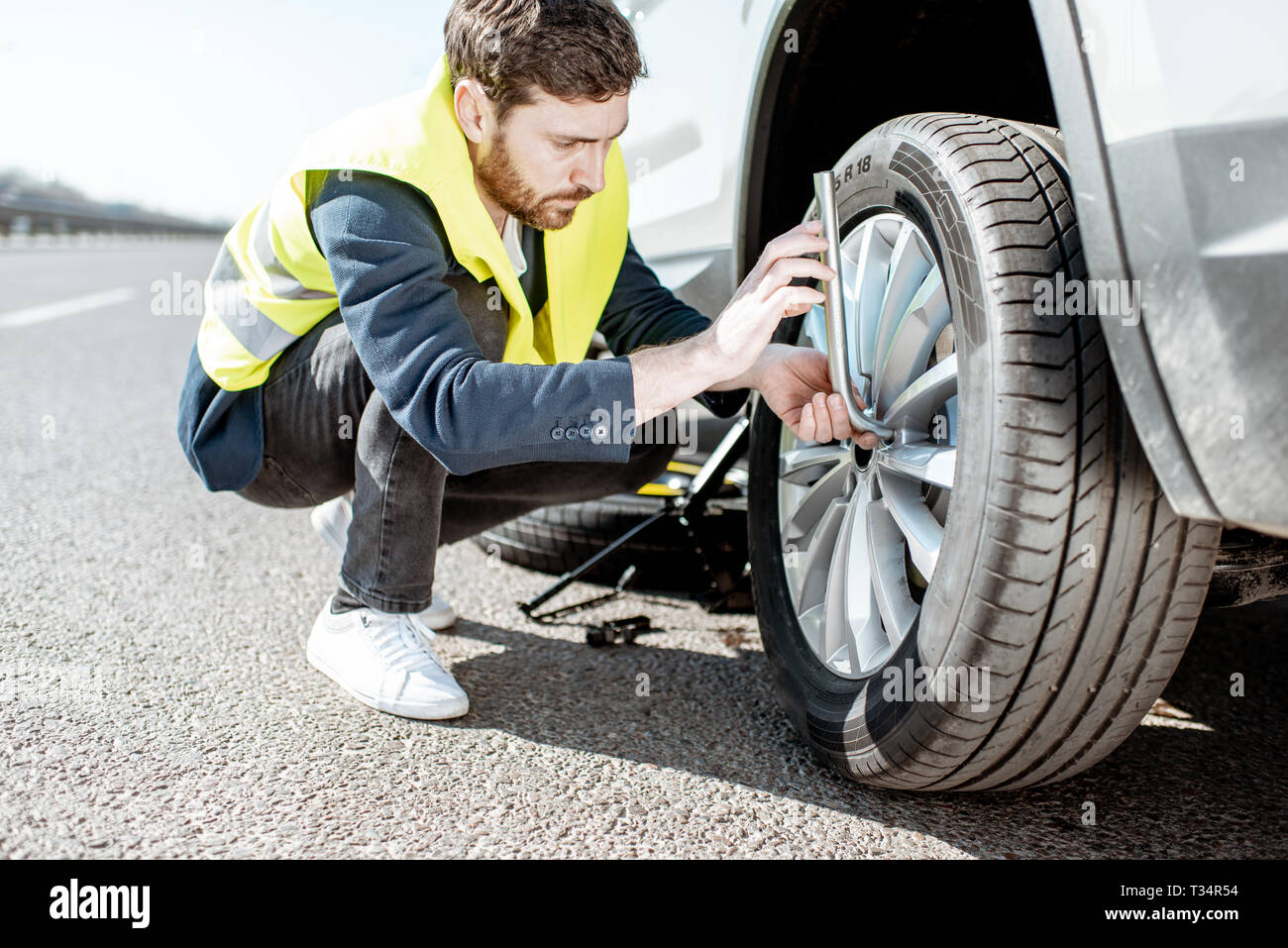 Uomo in vest svitando la ruota rotto sul ciglio della strada Foto Stock