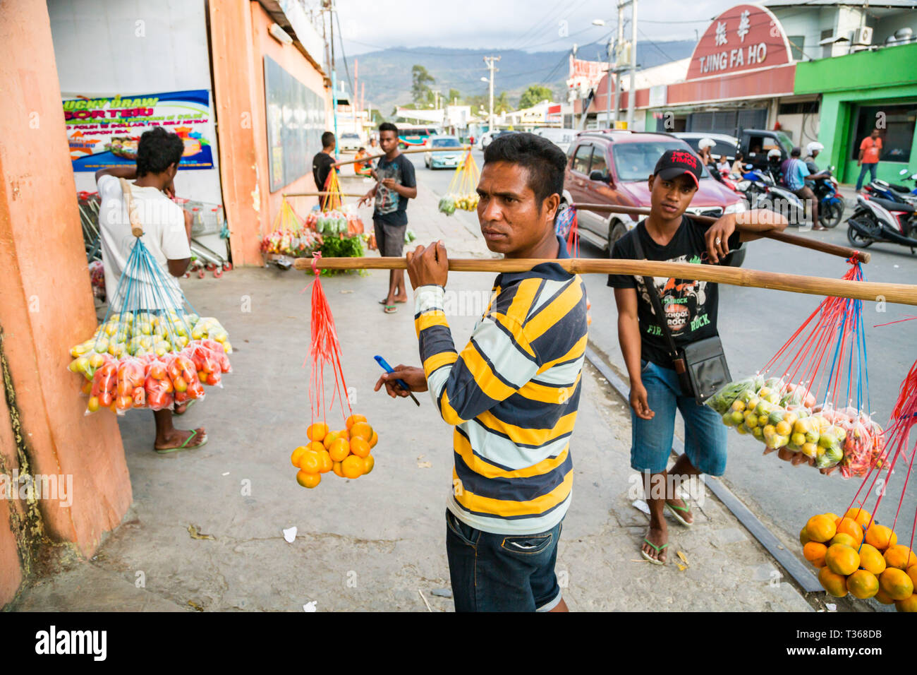 Gli uomini di Timor, street vending frutta e verdura appeso su funi dal collo gioghi fatta di bastoni in una trafficata strada del mercato del capitale Dili, Timor Est. Foto Stock
