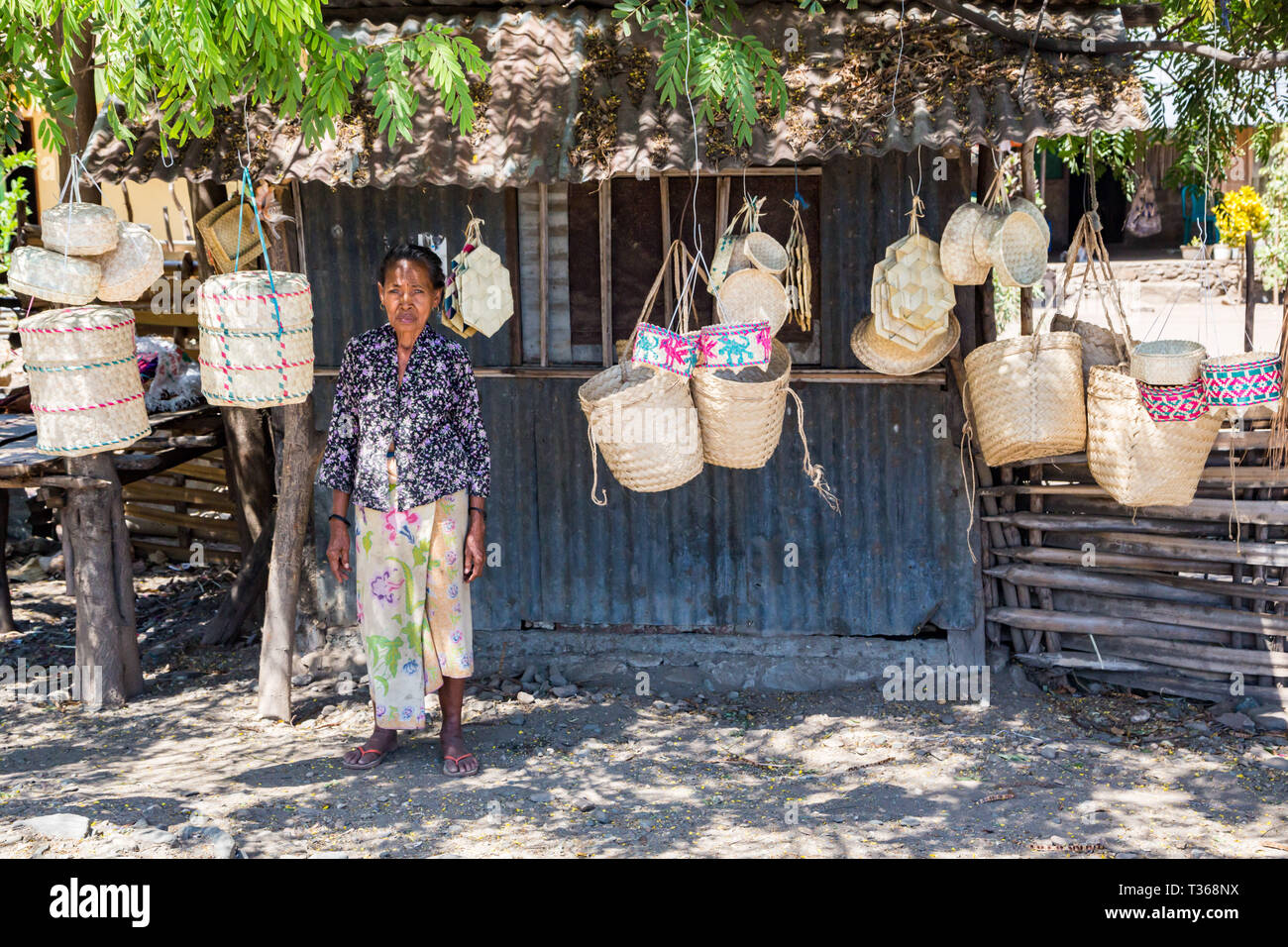Dili, Timor Est - 11 Ago, 2015: anziani locali nativi di Timor orientale donna, street vending tradizionali canestri di vimini appesi a funi, in corrispondenza di una capanna di stagno u Foto Stock