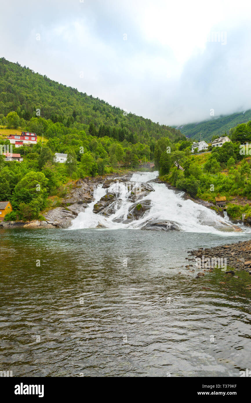 Case sul versante della montagna dal lago vicino alla cascata. Il fiume di montagna sfocia nel lago dalla cima della montagna. Foto Stock