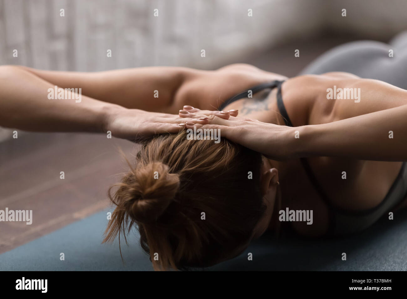 Giovane donna a praticare yoga, sdraiato a faccia in giù, collo Rafforzare esercizi Foto Stock