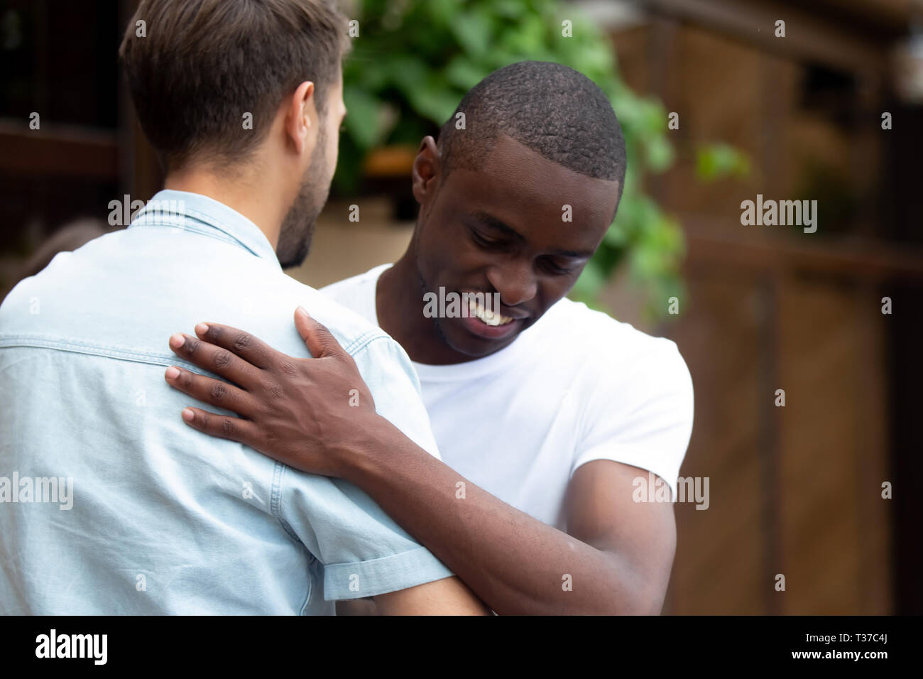 Felice due maschio e multirazziale migliori amici abbracciando il messaggio di saluto alla riunione Foto Stock