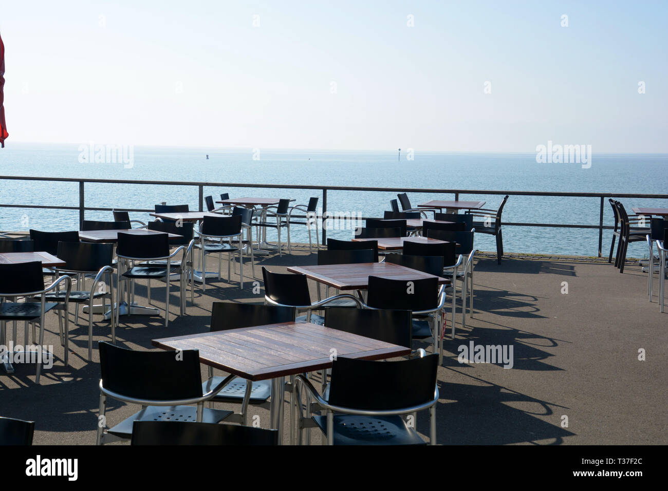 Svuotare cafe in primavera presso il lago di Costanza in Germania, tavoli e sedie senza persone sul lungolago contro il lago di Costanza e bouys Foto Stock