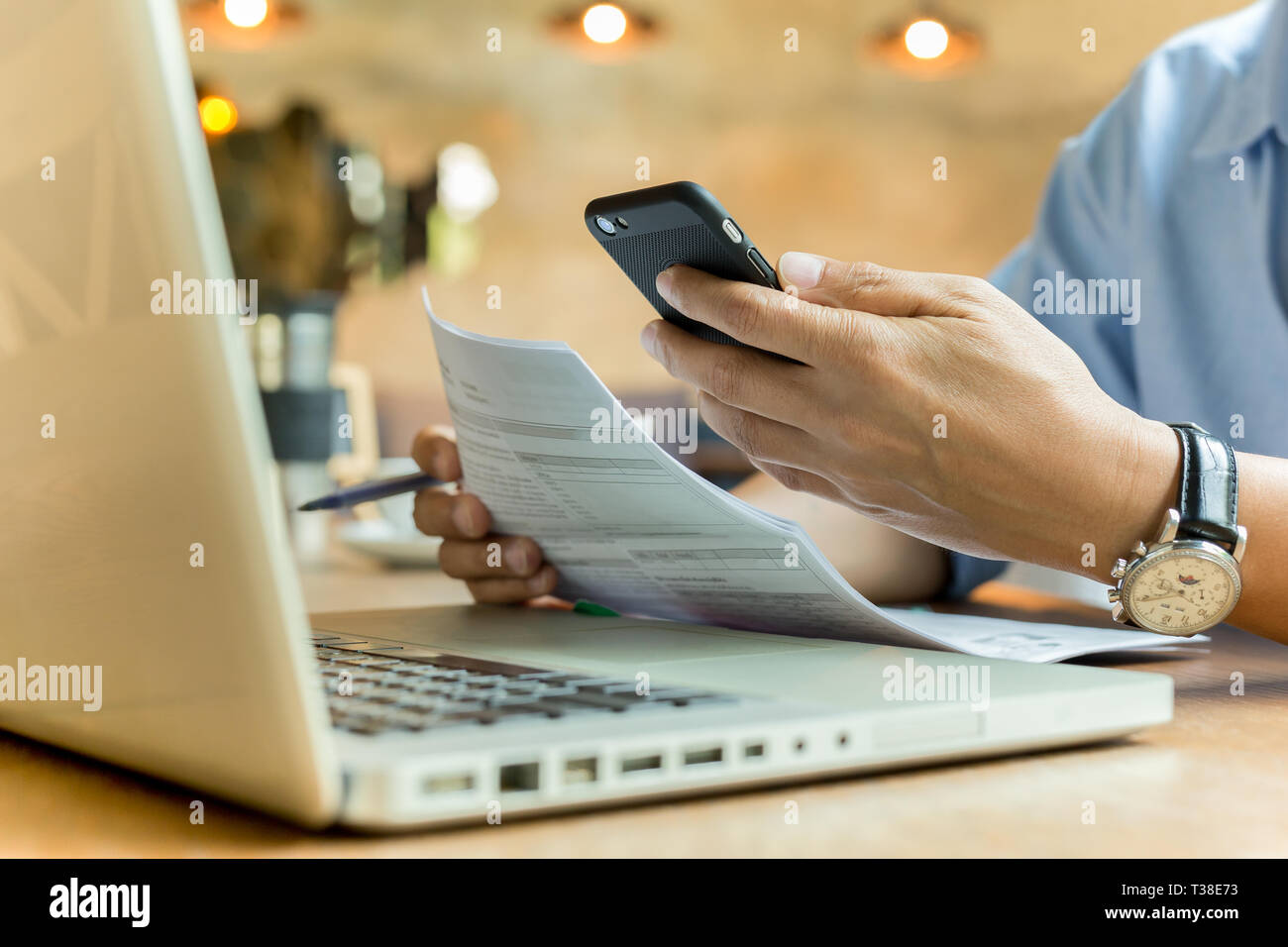 Uomo d'affari tramite telefono cellulare e documento di contenimento con il computer portatile sul tavolo. Foto Stock