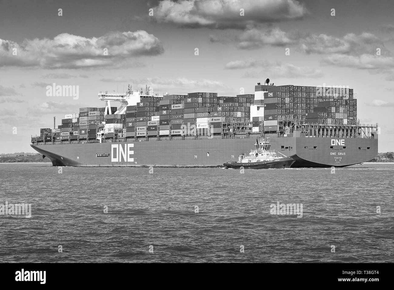 Foto in bianco e nero di Tug PHENIX che guida la nuova nave portacontainer Ocean Network Express, ONE GRUS, mentre si avvicina al porto di Southampton, Regno Unito. Foto Stock