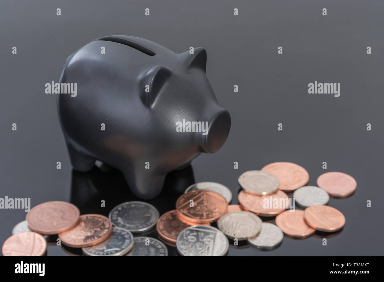 Ceramica Nera salvadanaio con monete del Regno Unito riflettente su sfondo nero. Metafora per il risparmio di denaro, risparmi personali. Foto Stock
