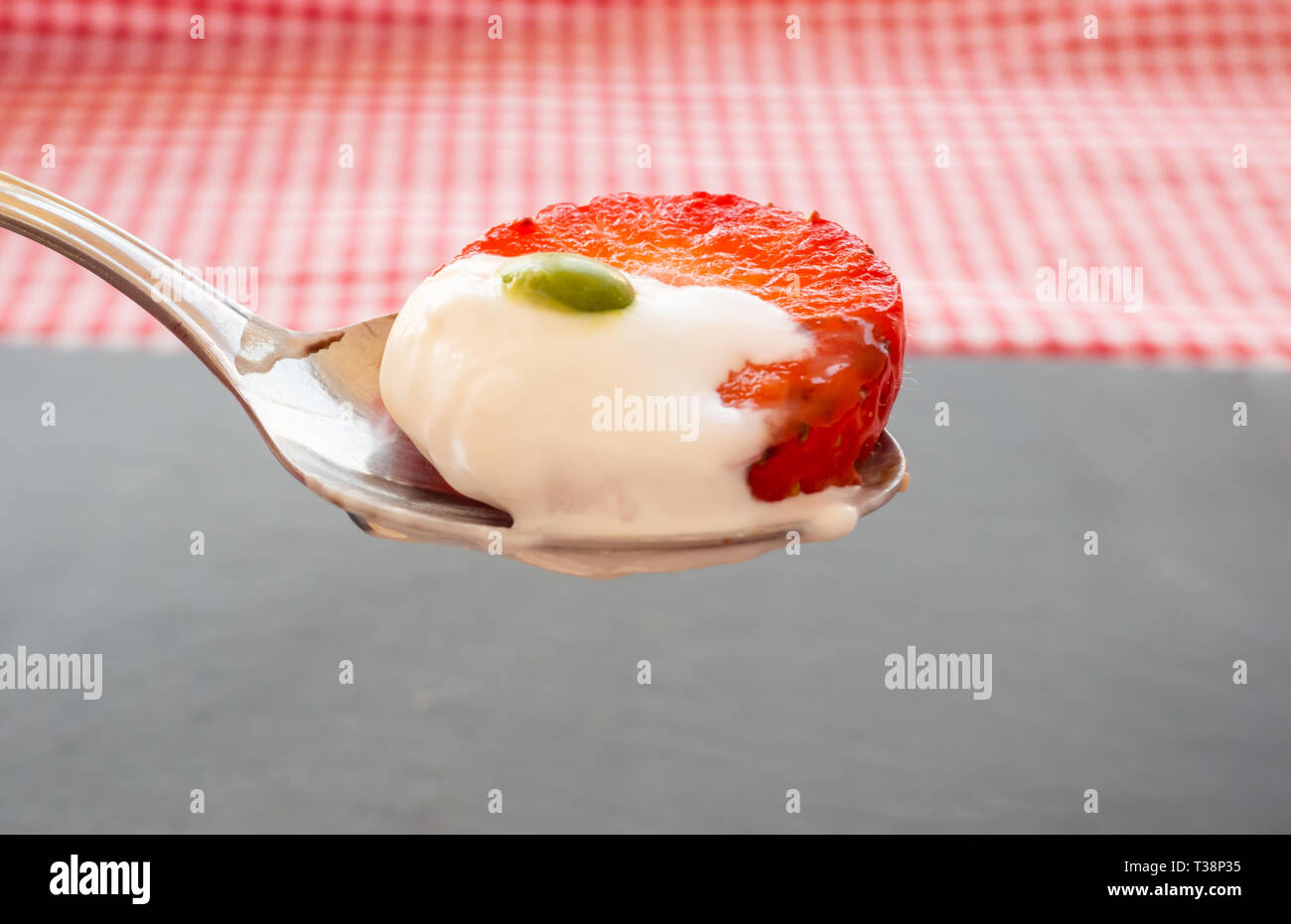 Un cucchiaio in mano con crema, un colore del cioccolato e un pezzo di fragola Foto Stock
