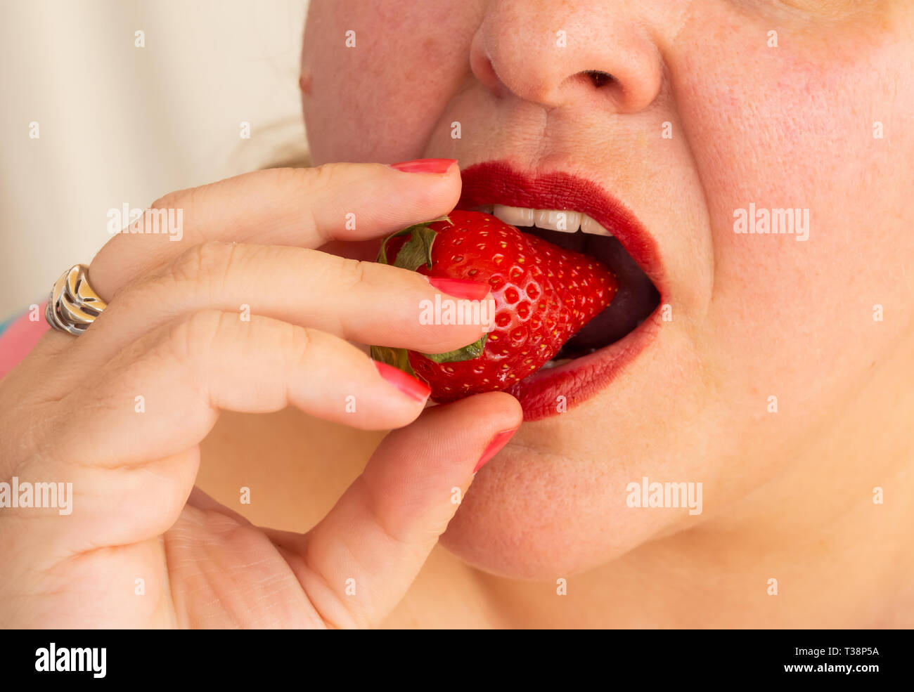 Una donna adulta con unghie rosse e le labbra di mangiare una fragola Foto Stock
