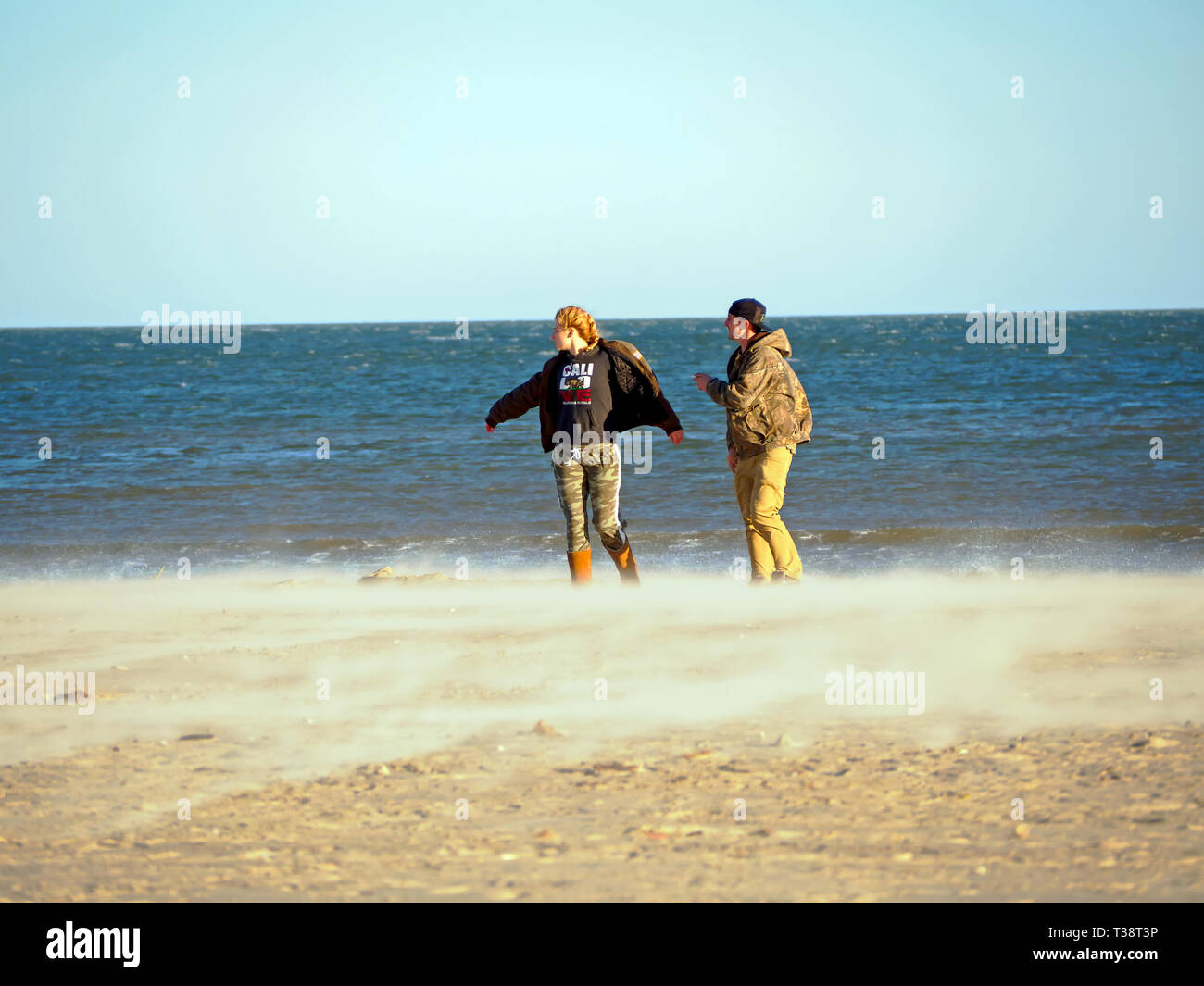 Una giovane donna e compagno maschio sperimentare il freddo, ventoso, Gennaio beach in Port Aransas, Texas, Stati Uniti d'America. Foto Stock