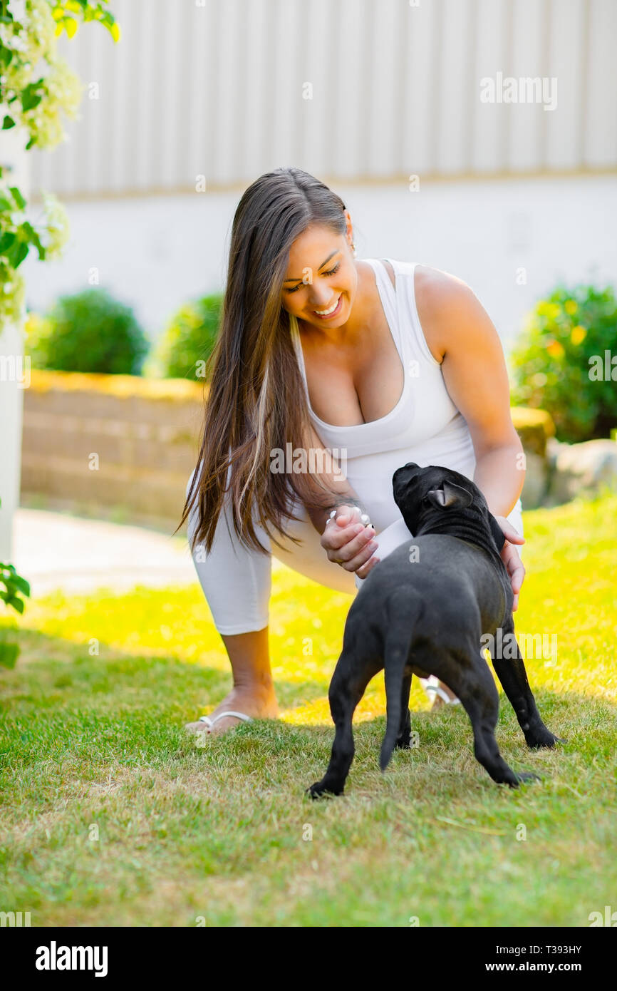 Allegra donna incinta con una grande pancia gioca con il suo cane in giardino Foto Stock