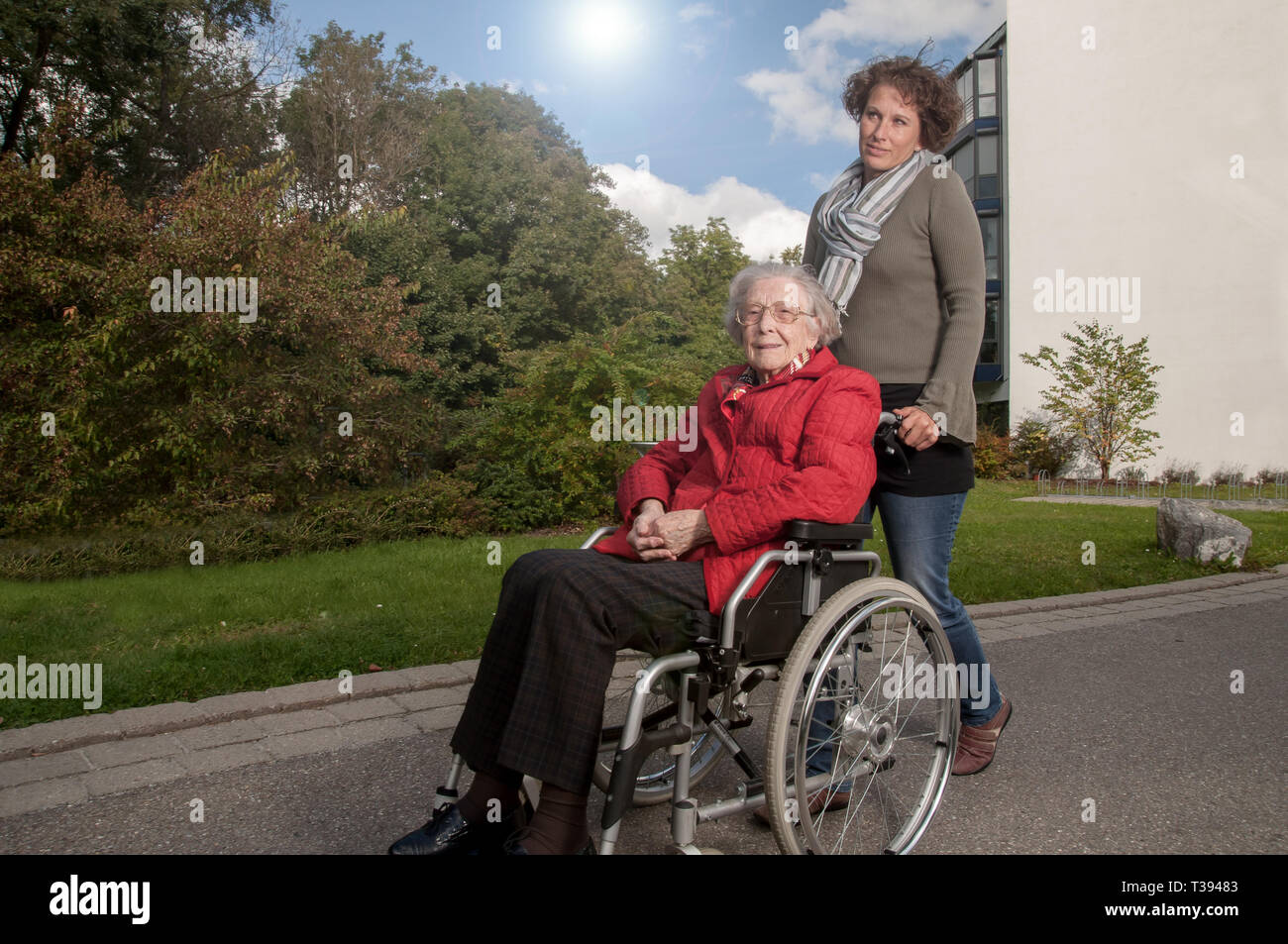 Giovane donna aiuta donna senior in carrozzella Foto Stock