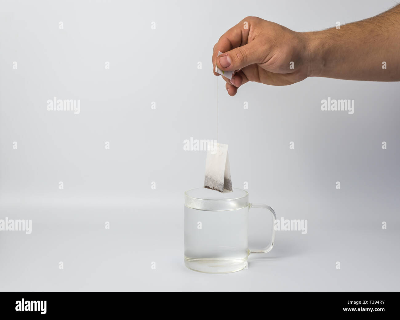 Mano con un sacchetto da tè e la coppa di vetro con acqua bollente Foto Stock