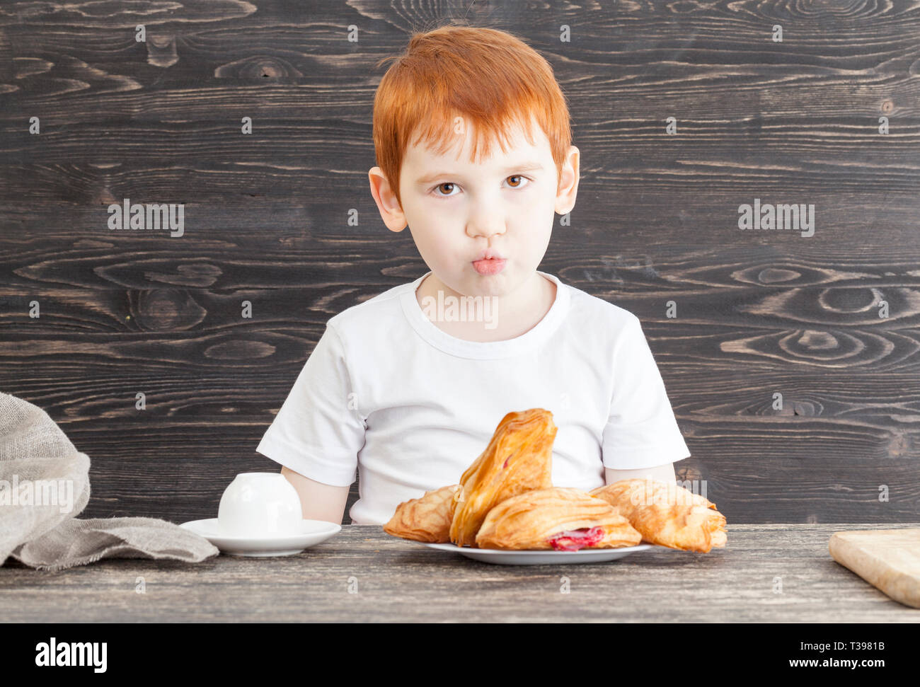 Ragazzo seduto al tavolo con un gustoso panino con red cherry riempimento, snack dolce, non dietetici alimenti nocivi Foto Stock