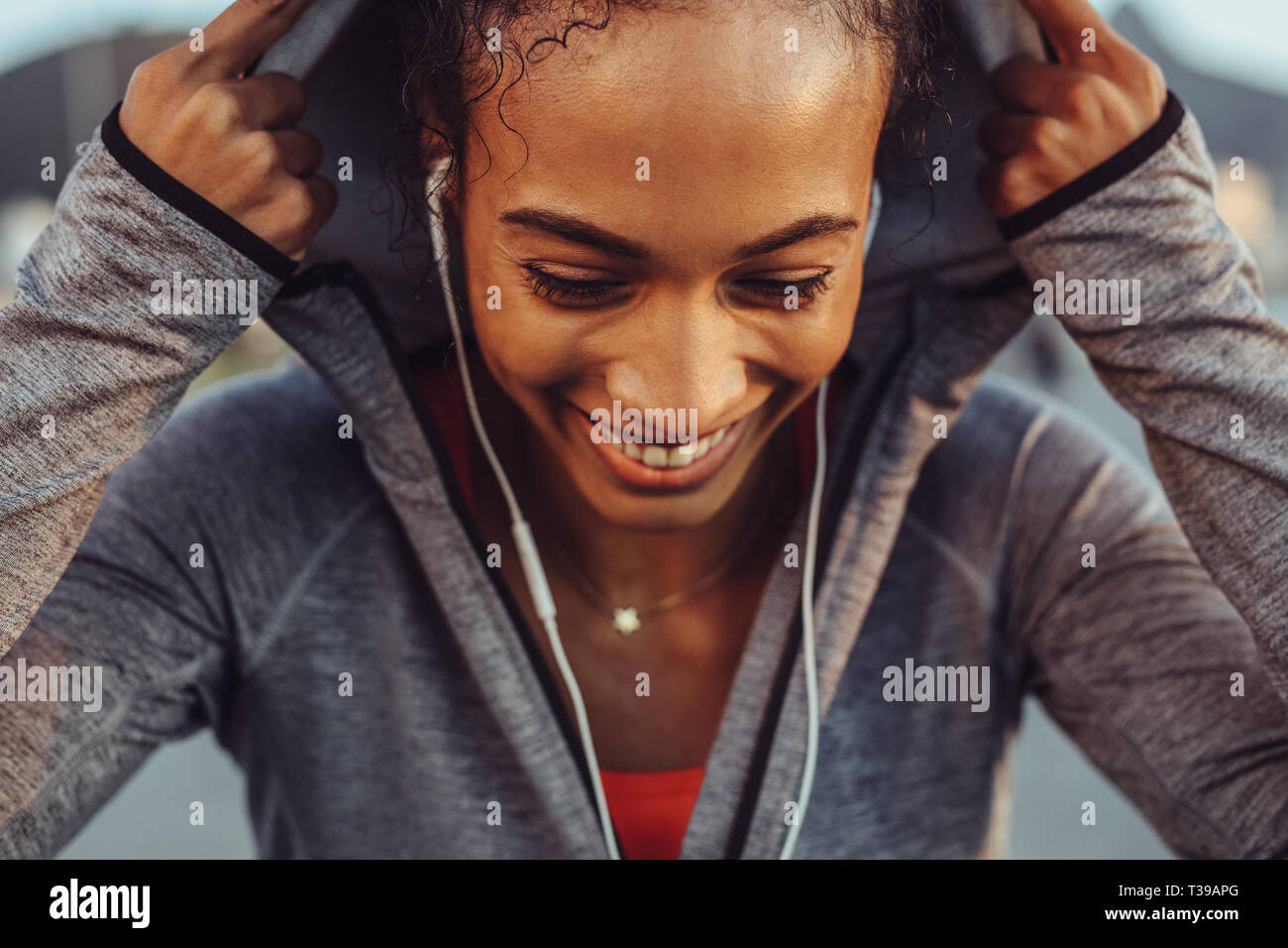 Close up di montare la giovane donna che indossa una felpa con cappuccio sorridente all'esterno. Pareggiatore femmina facendo riposare dopo una corsa. Foto Stock