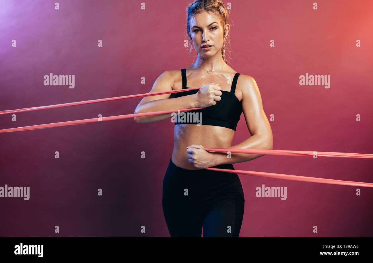 Donna tenace resistenza utilizzando bande nel suo esercizio di routine. Atleta femminile esercitando con banda di resistenza contro lo sfondo colorato. Foto Stock