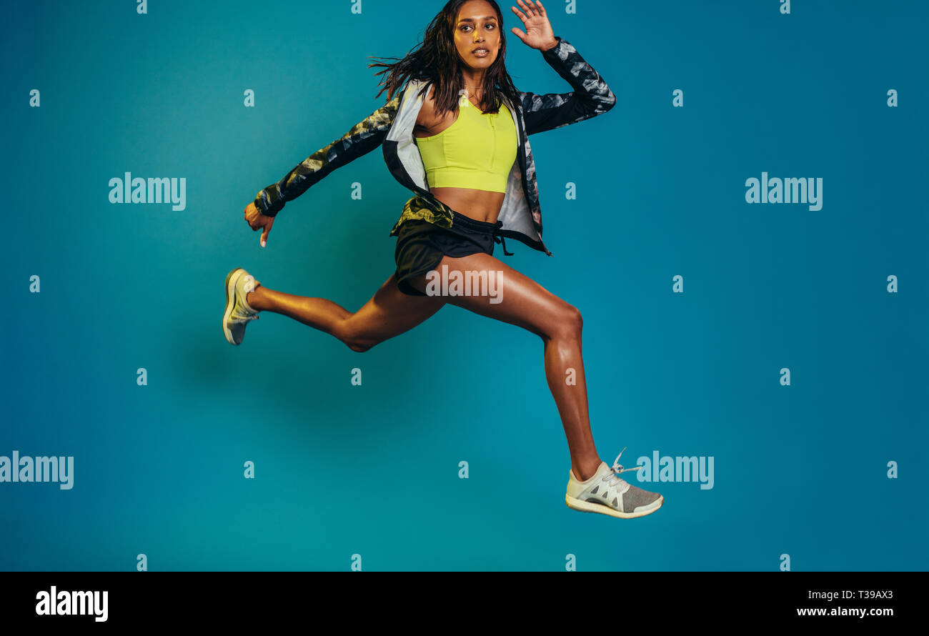 Lunghezza completa di sano giovane donna di salto e in esecuzione. Giovani femmine runner training su sfondo blu. Foto Stock