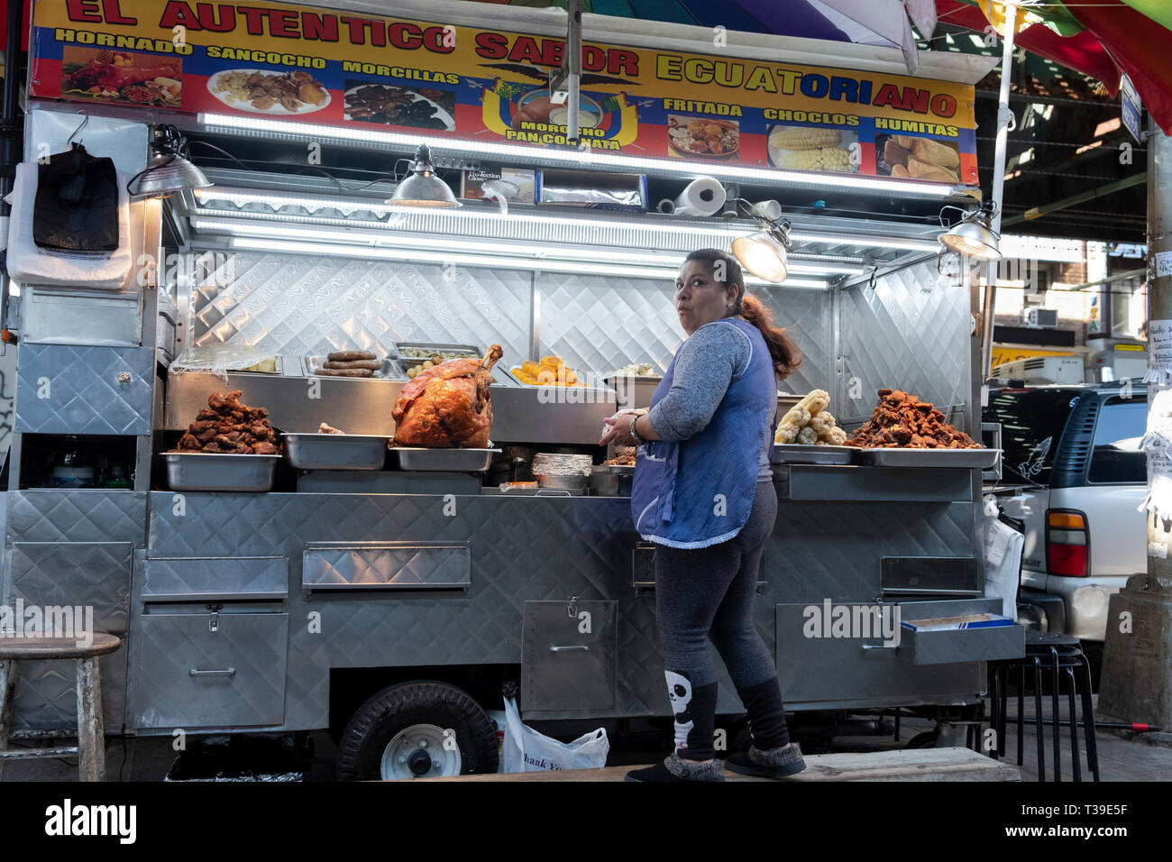 Un ecuadoriano donna americana la vendita di carni alla griglia e altri alimenti da un carrello sotto la sopraelevata treni della metropolitana . In corona, Queens, NYC Foto Stock