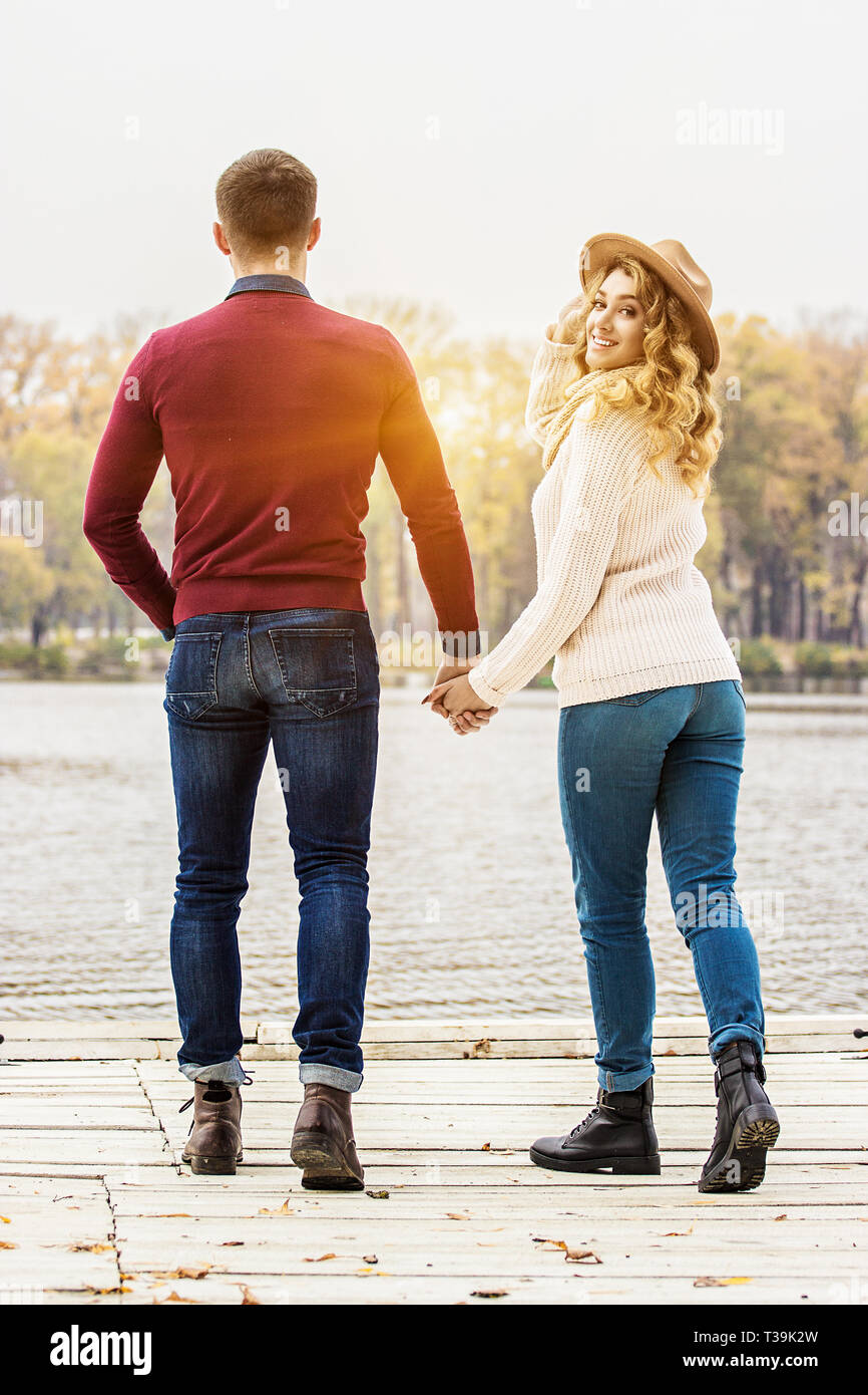 Per sempre insieme. Vista posteriore del giovane e bella giovane in abbigliamento casual mantenendo le mani insieme mentre passeggiate all'aperto. Donna che guarda alla telecamera. Coupl Foto Stock