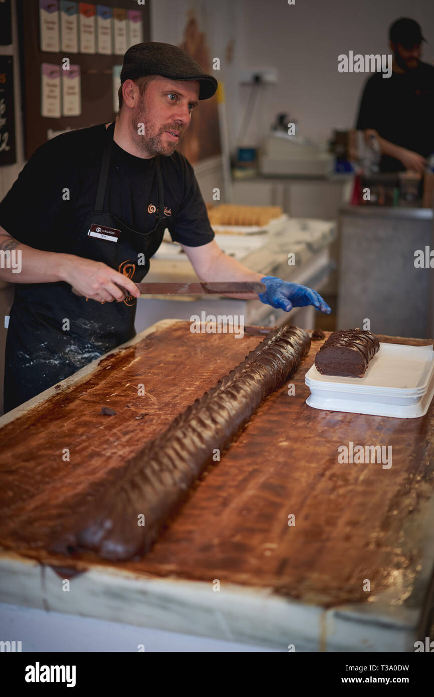 Cambridge, Regno Unito - dicembre, 2018. Un uomo la preparazione di fudge tradizionale in una panetteria. Fudge è un tipo di zucchero candito realizzato miscelando lo zucchero, il burro e il latte. Foto Stock