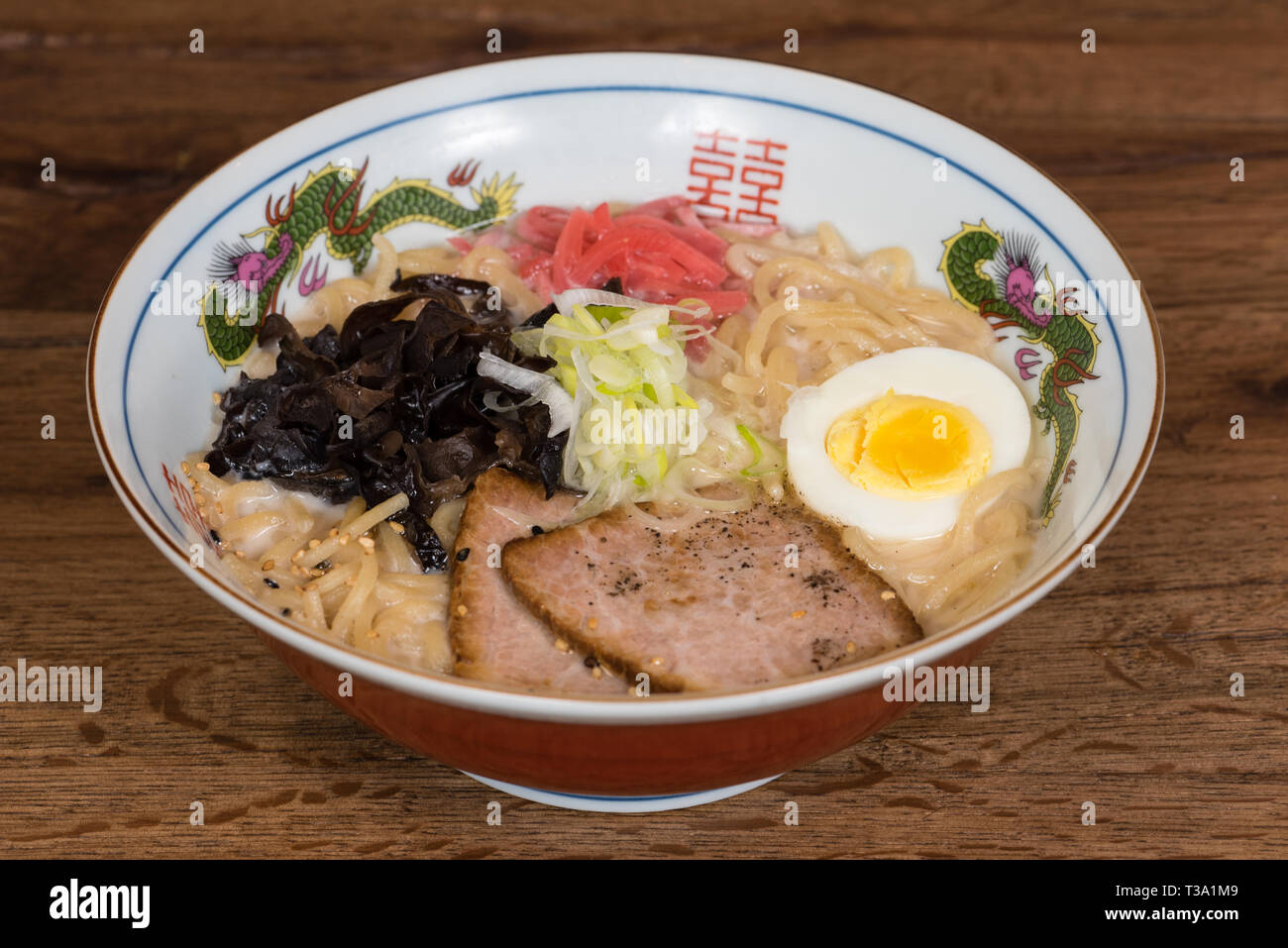 Ramen tonkotsu con carne di maiale, latte di soia, brodo di carne di maiale, funghi neri, uova, cipolle, servita in una ciotola di legno scuro dello sfondo della tabella Foto Stock