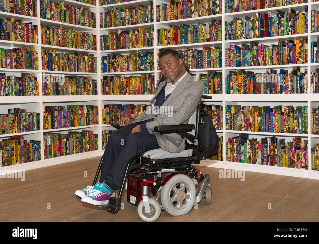 Londra, Regno Unito. 8 Aprile, 2019. L'artista Yinka Shonibare CBE, alla Tate Modern accanto alla sua installazione la British Library, le ultime opere d'arte di essere acquisita da Tate.La British Library è un sito-specifica installazione con una piattaforma digitale per i visitatori a partecipare alla discussione. Una celebrazione della diversità della popolazione britannica contiene 6,328 libri rilegati in "dutch cera stampa', un tessuto caratteristicamente usati dall'artista nel suo lavoro. Credito: Malcolm Park/Alamy Live News. Foto Stock