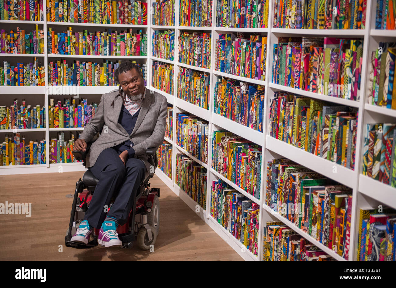 Londra, Regno Unito. 8 Aprile, 2019. L'artista Yinka Shonibare CBE, alla Tate Modern accanto alla sua installazione la British Library, le ultime opere d'arte di essere acquisita da Tate.La British Library è un sito-specifica installazione con una piattaforma digitale per i visitatori a partecipare alla discussione. Una celebrazione della diversità della popolazione britannica contiene 6,328 libri rilegati in "dutch cera stampa', un tessuto caratteristicamente usati dall'artista nel suo lavoro. Credito: Malcolm Park/Alamy Live News. Foto Stock