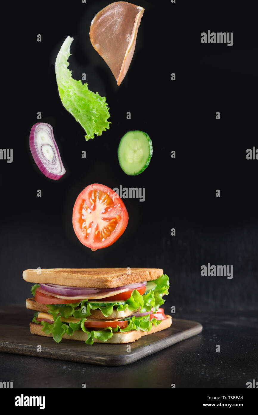 Flying ortaggi per sandwich gustosi , bacon, pomodoro, cipolla, insalata su sfondo nero. Isolato Foto Stock