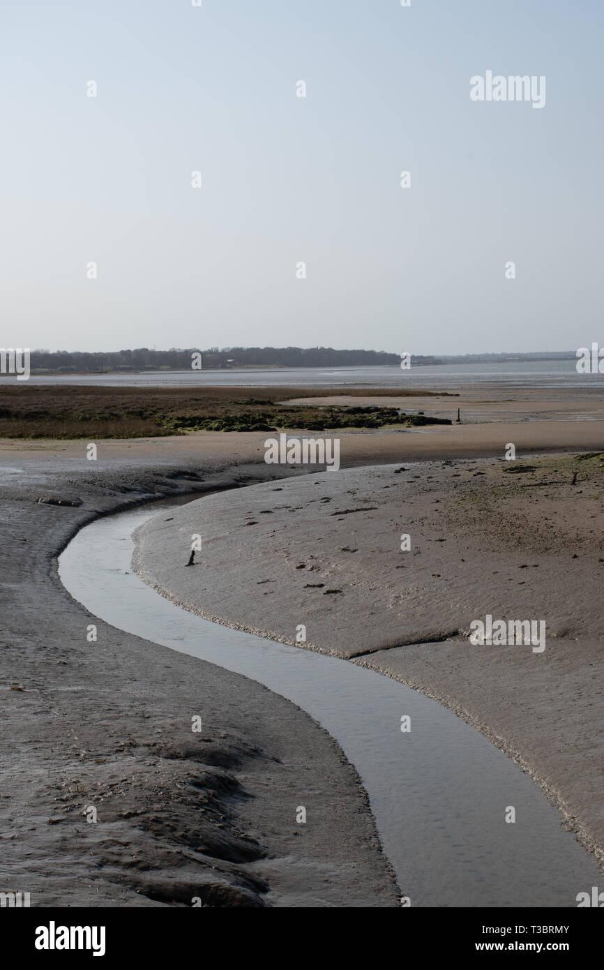 Flusso di avvolgimento voce a mare nel fangoso estuario del regno unito a bassa marea con cielo chiaro Foto Stock