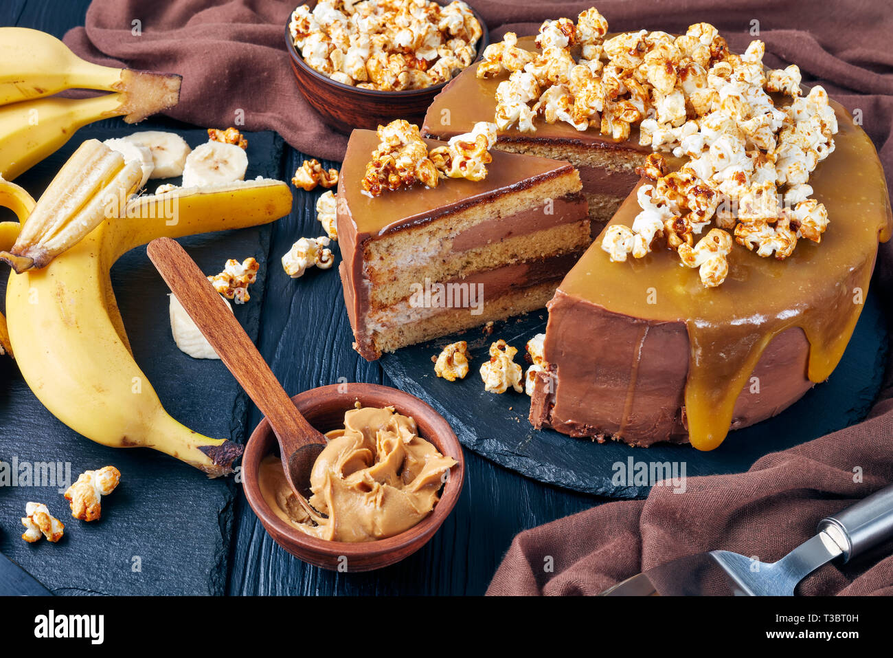 Fette di banana pan di spagna a strati con burro di arachidi mousse e guarnita con glassa al cioccolato fuso caramello e popcorn dolce, vista orizzontale da Foto Stock