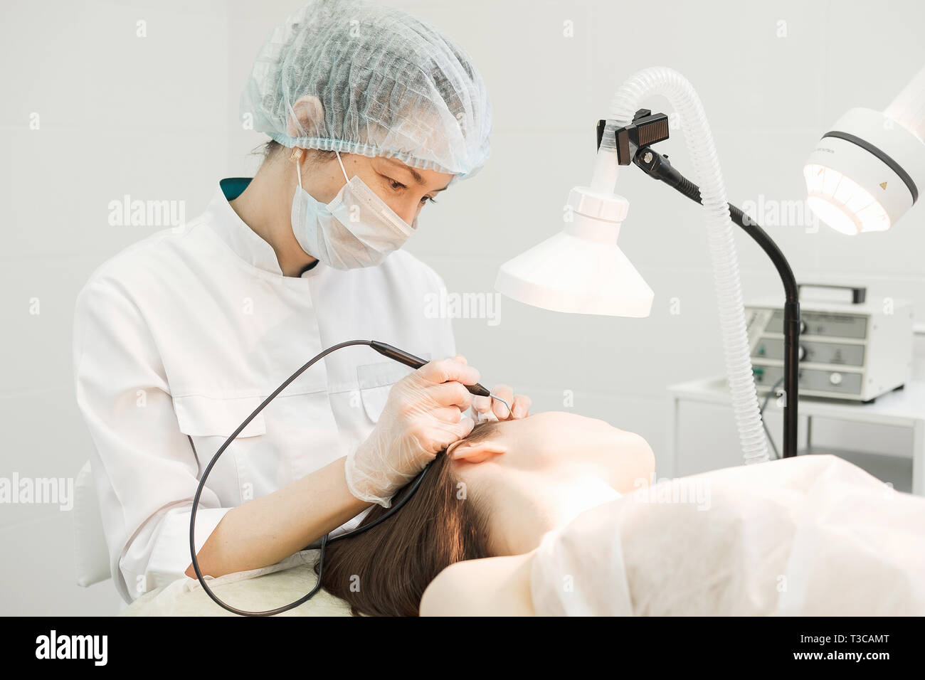 Trattamento medico la rimozione di birthmark femmina dal viso del paziente. Femmina dermatologo chirurgo utilizzando un professionista di elettrocauterizzazione per la rimozione di mole. Foto Stock