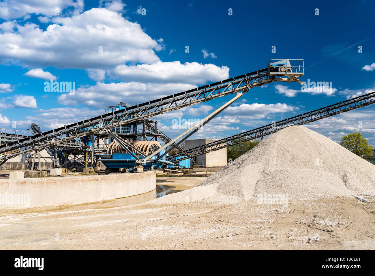 Il convogliatore su cumuli di ghiaia sul cielo blu in corrispondenza di un settore industriale impianto di cemento. Foto Stock